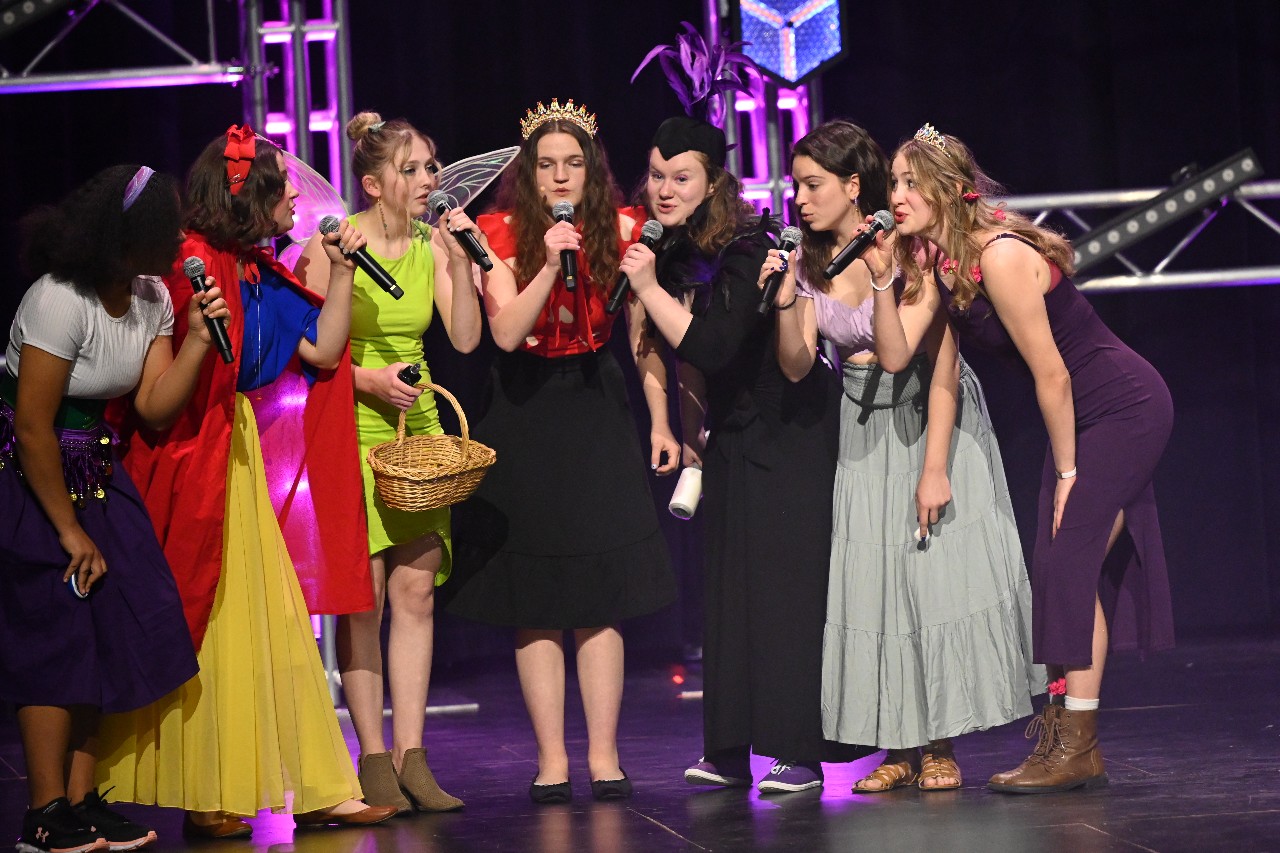 Students dressed as villains and princesses, lean in while singing on stage