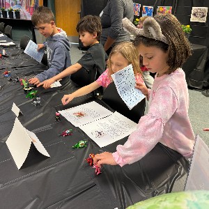 Students look at small toys on a table.