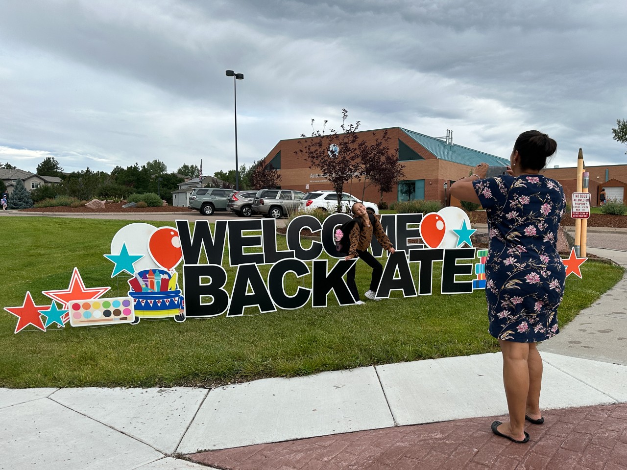 A mom takes a photo of her student near a sign that reads Welcome back ATE!