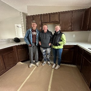 Three people smile for a photo in an empty kitchen