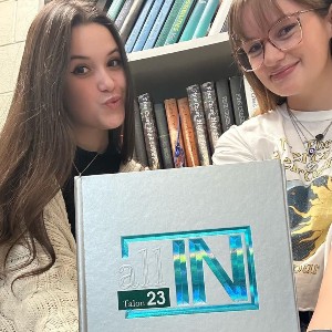 Students holding a yearbook with the words "All IN" on the cover