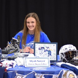 Aliyah Sawyer smiles for the camera in front of a table decorated with hockey gear.