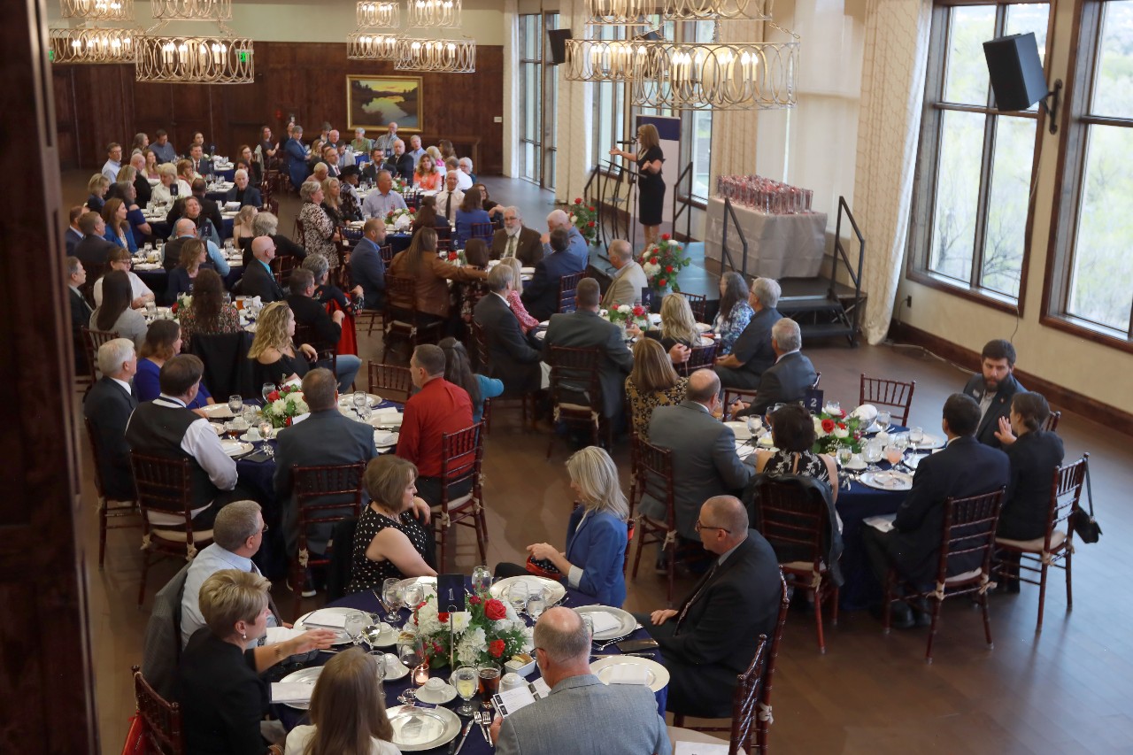 A dining room is filled with 2023 Retiree Banquet attendees while Allison Cortez, emcee for the night, stands at a podium and kicks off the event