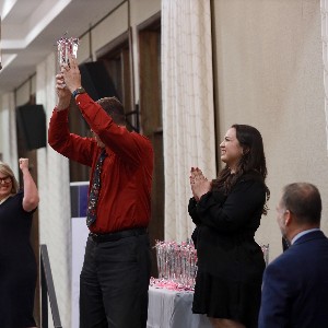 Jeffrey Keller celebrates his retirement by holding up his glass vase in celebration while watchers cheer him on