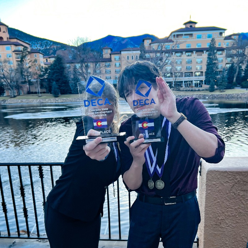 Josh and Mackenzie pose with their trophies, their eyes peeking through the DECA logo
