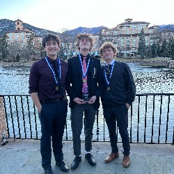 Three boys pose with their medals and trophy