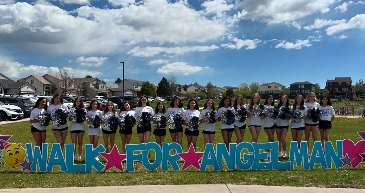 Cheerleaders group shot in front of Walk For Angelman sign