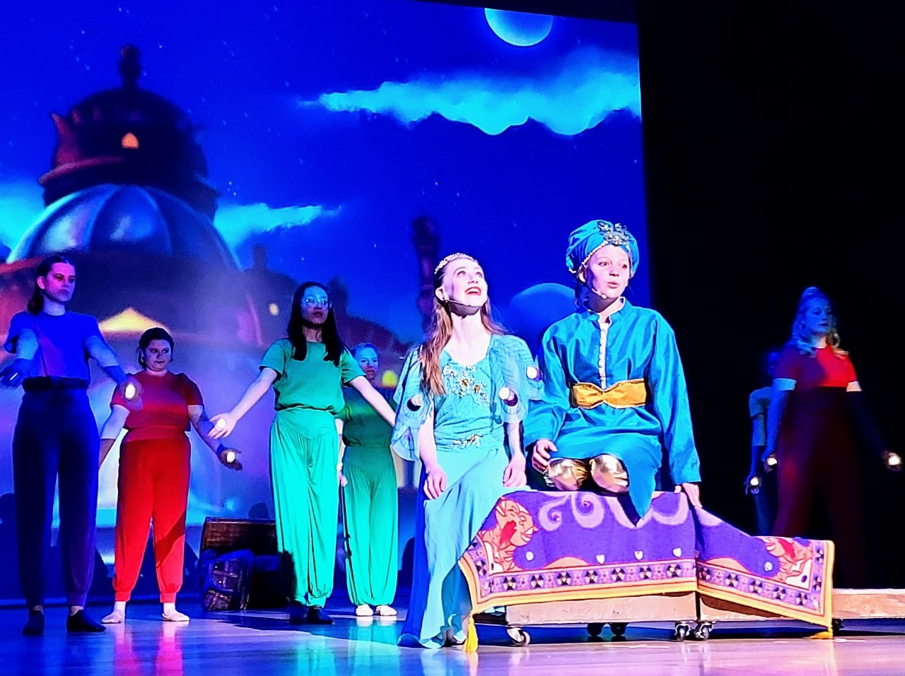 Students on stage riding a magic carpet.