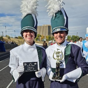 Two marching band students pose with trophies