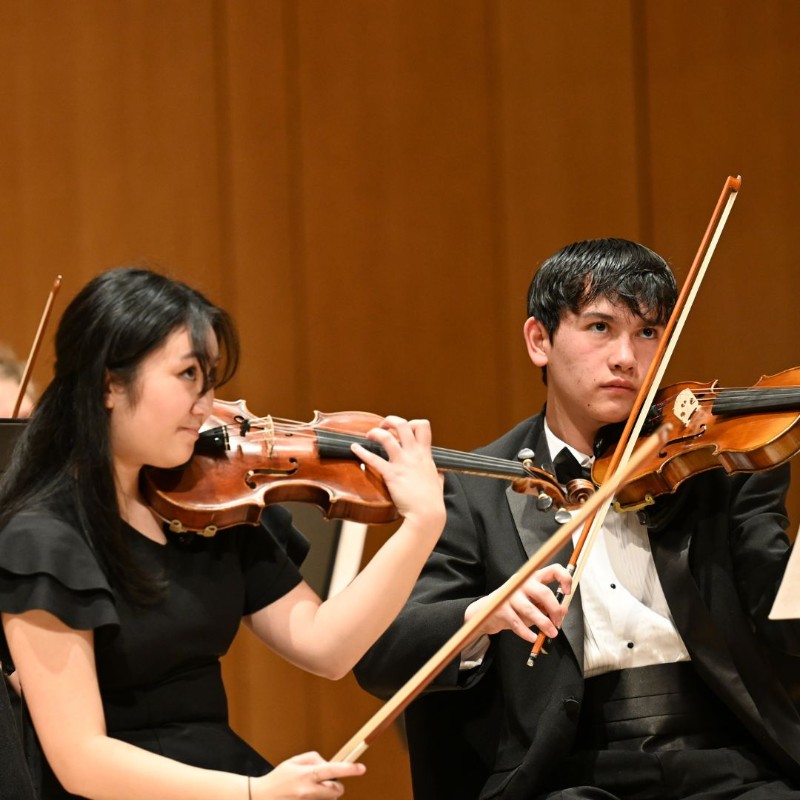 Students playing violin looking up at conductor