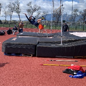 Athlete sticking pole into the mat to fling himself over the pole vault bar