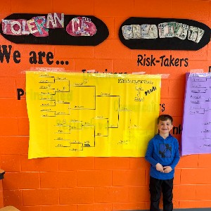 A smiling student standing by a tournament bracket.