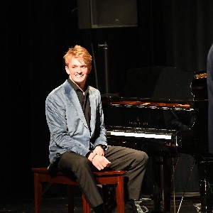 Student seated at piano, smiling