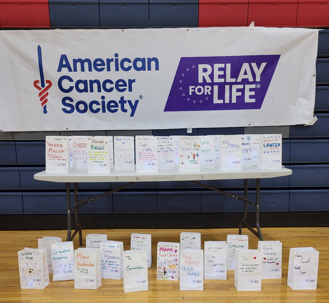 Luminaria bags sit on and in front of a table with an American Cancer Society Relay for Life banner.