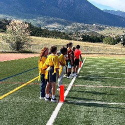 Flag football players wait on the sideline. The background includes the Rocky Mountains.