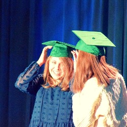 Best friends wearing graduation caps smile at each other 