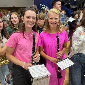 Two clarinet players wearing pink smile for the camera