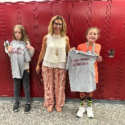 Students holding Eagleview Athletics t-shirts stand with Mrs. White in front of lockers.