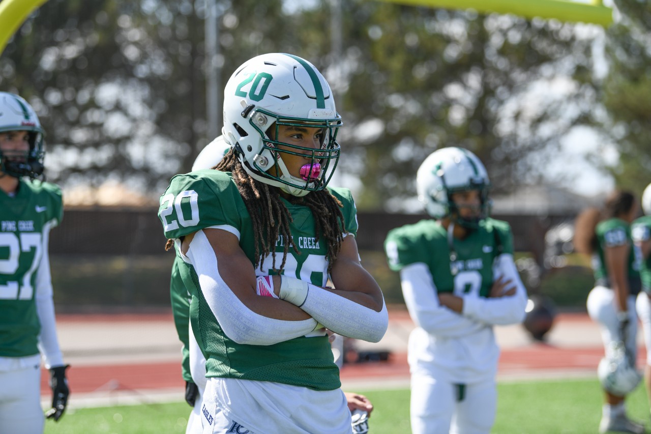 #20 stands on the sideline with arms crossed over chest