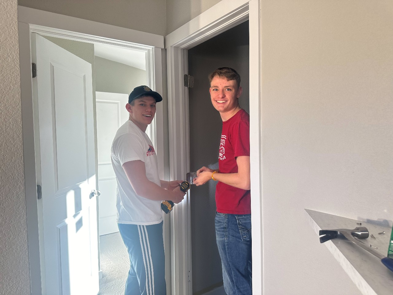Two current D20 construction students use a screwdriver on a door frame in the modular home they help build.