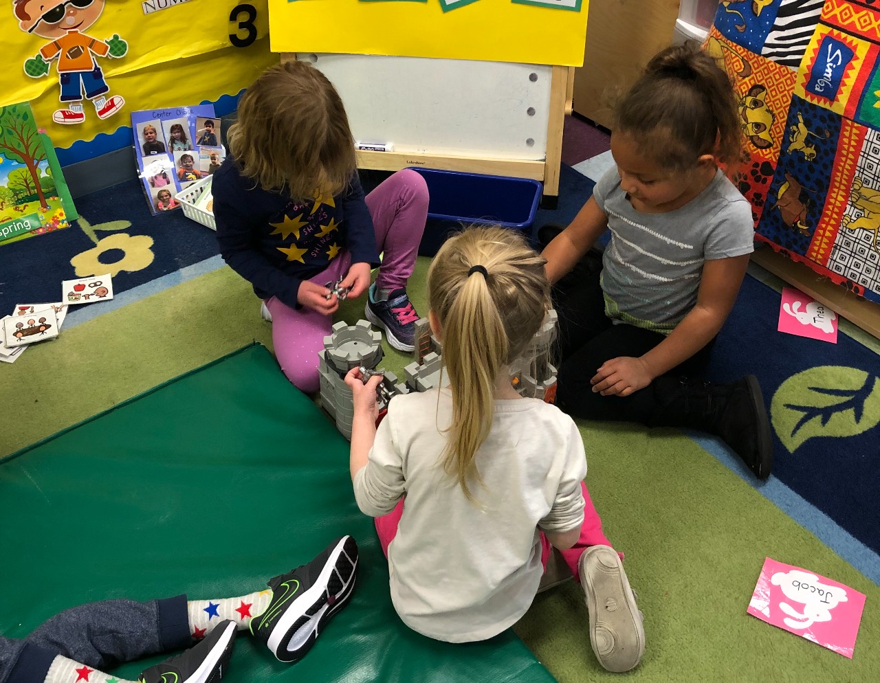 Three preschool students assemble a lego castle on the floor.