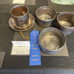 1st place ribbon next to three silver bowls and silver cup with saucer