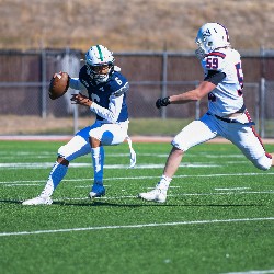 #6 preparing to throw the football before being tackled by approaching player from the opposite team