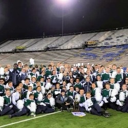 Marching band members pose on the field after a performance.