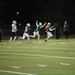 Player runs the ball into the end zone for a touchdown and teammate behind him throws his arms up in celebration.