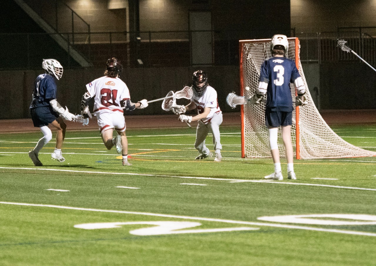 Boys lacrosse player throws ball towards the goal.