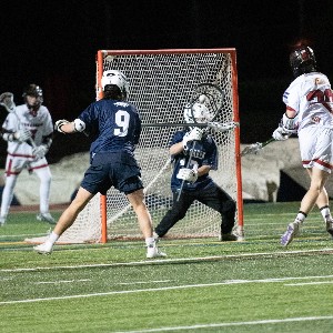 Boys lacrosse players defend the goal.