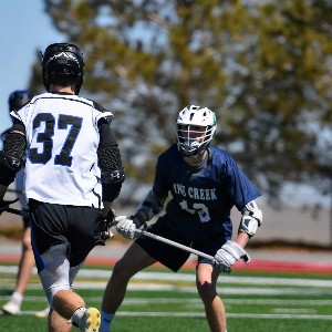 Boys lacrosse player confronts that athlete carrying the ball.