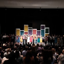 Cast holding hands and taking a bow at the end of the performance while the audience gives a standing ovation.
