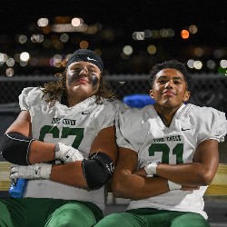 Two players pose for the camera from the sidelines with arms crossed over chest