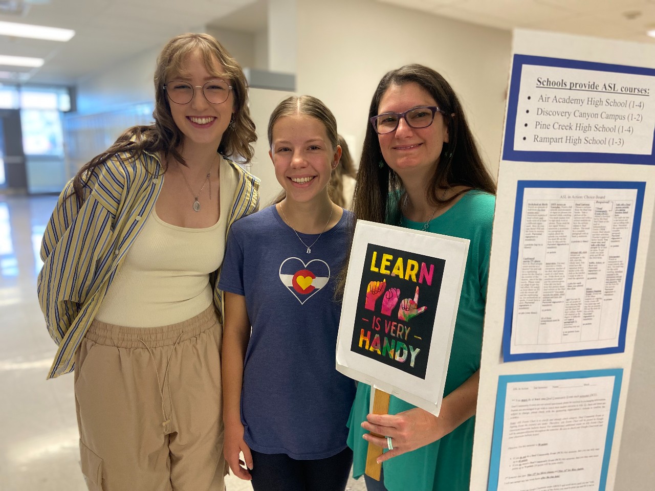 Two students and a teacher stand by AAHS ASL club station