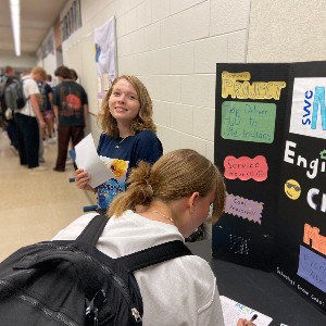 Student stands by Engineering Club trifold while another student fills out sign up form.