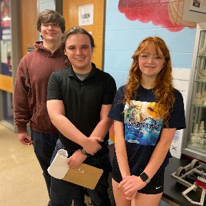 Three students stand by Robotics Club station