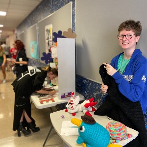 Crafting club student volunteer smiles at camera while crocheting