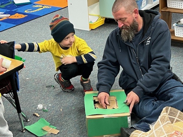 Building manager helps a student cut cardboard.