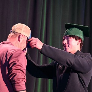 Student putting ballcap on a man