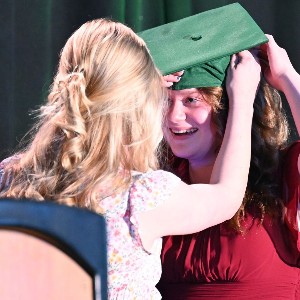 Two sisters smile at each other while trying to get Graduation cap on.