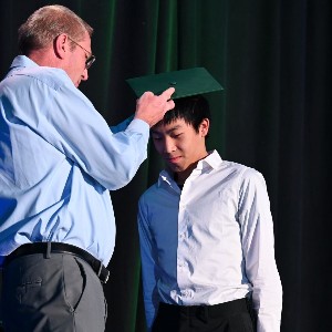 Teacher putting Graduation cap on student.