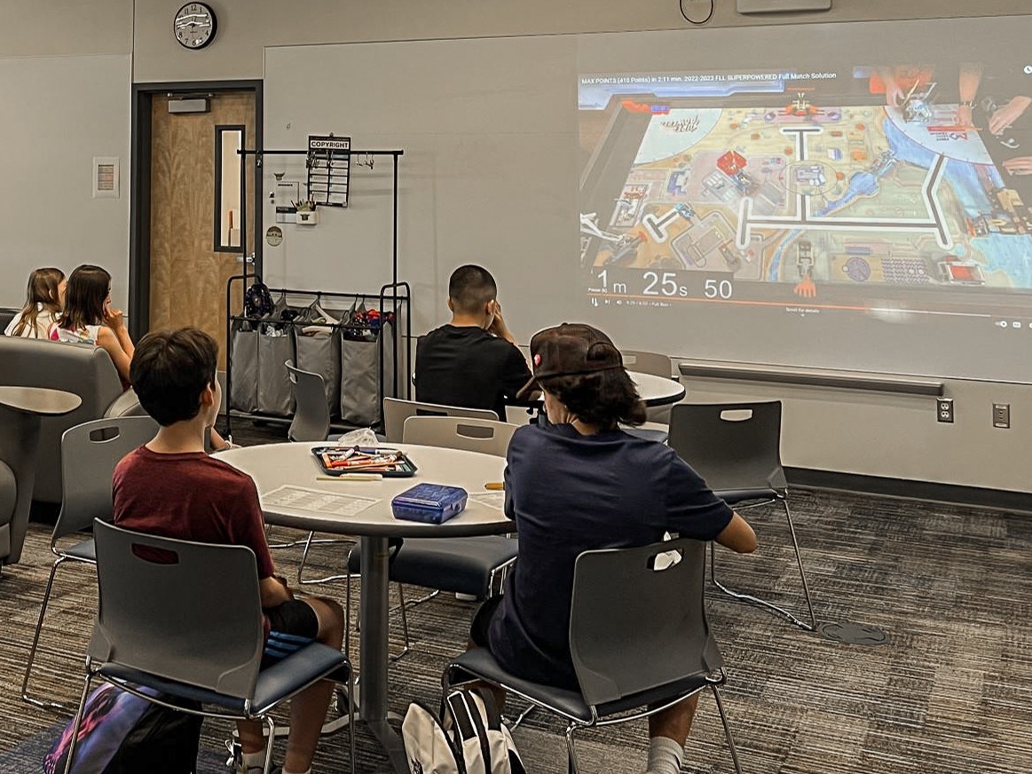 Students in a common room, watching an internet video of a game.