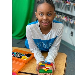 A student smiles as she shows off her lego creation.