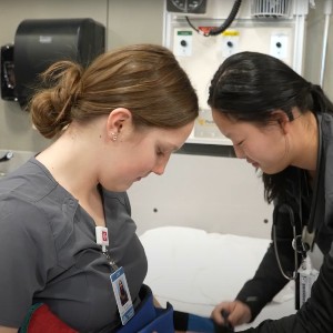 Two students practice the use of a blood pressure cuff.