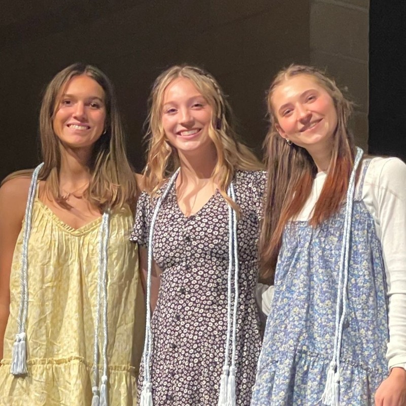 Three students wearing honor cords, smile at the camera