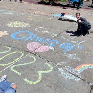 Student poses near sidewalk chalk that reads, "Congrats, Class of 2023!"