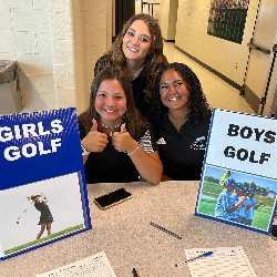 Students pose by signs labeled "Girls Golf" and "Boys Golf"