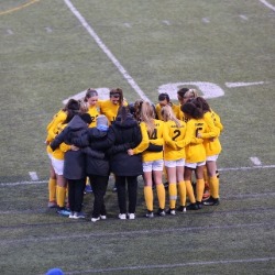 The RHS Girls Soccer team huddles on the field.