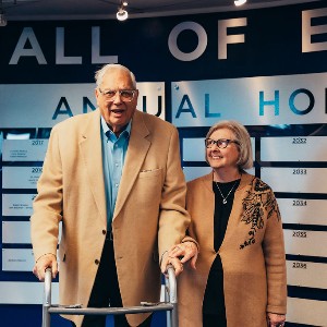 Bob Cohn with his wife in front of the Hall of Excellence wall